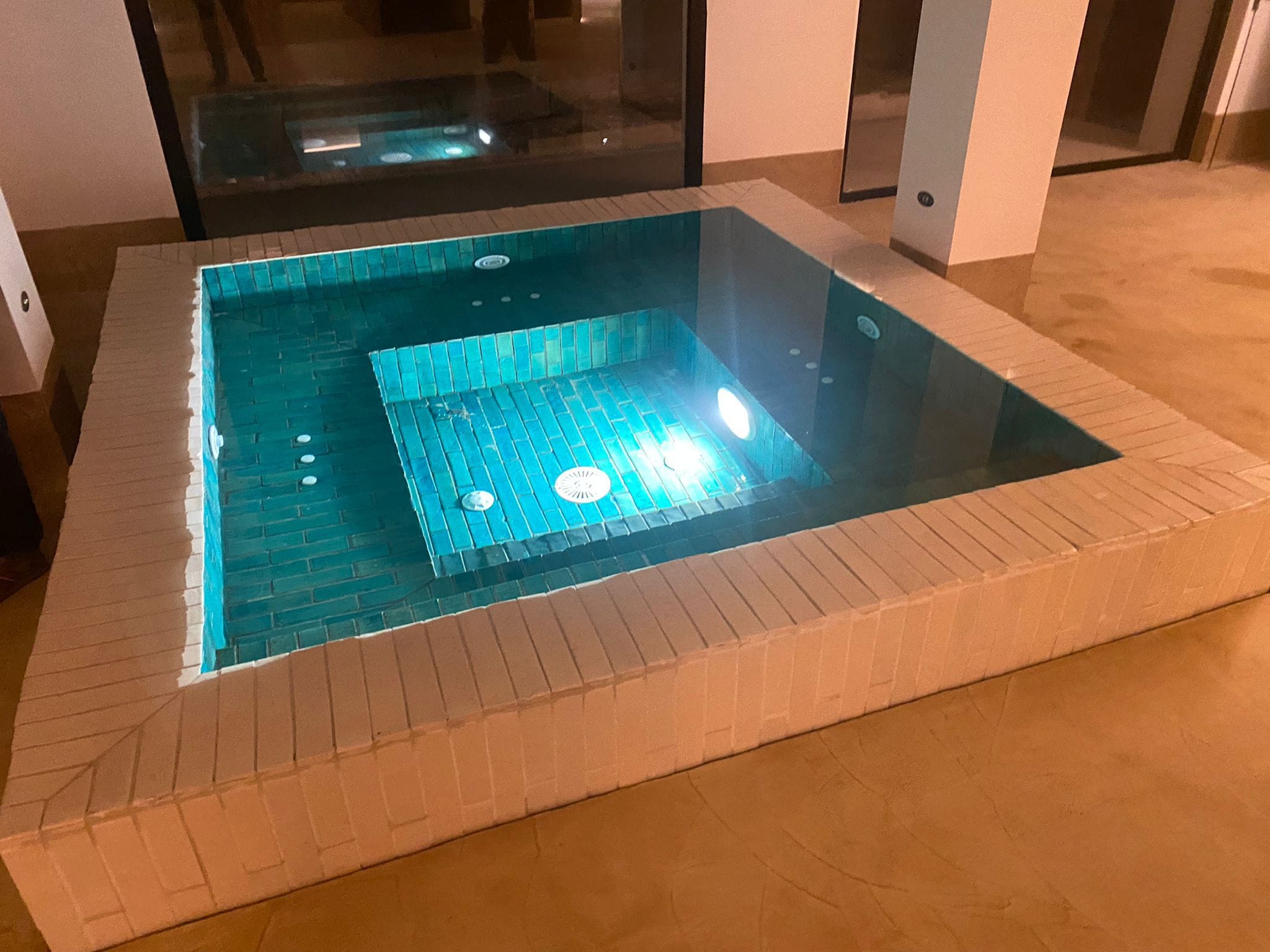 A square hot tub with a tiled surround and a glass enclosure.
