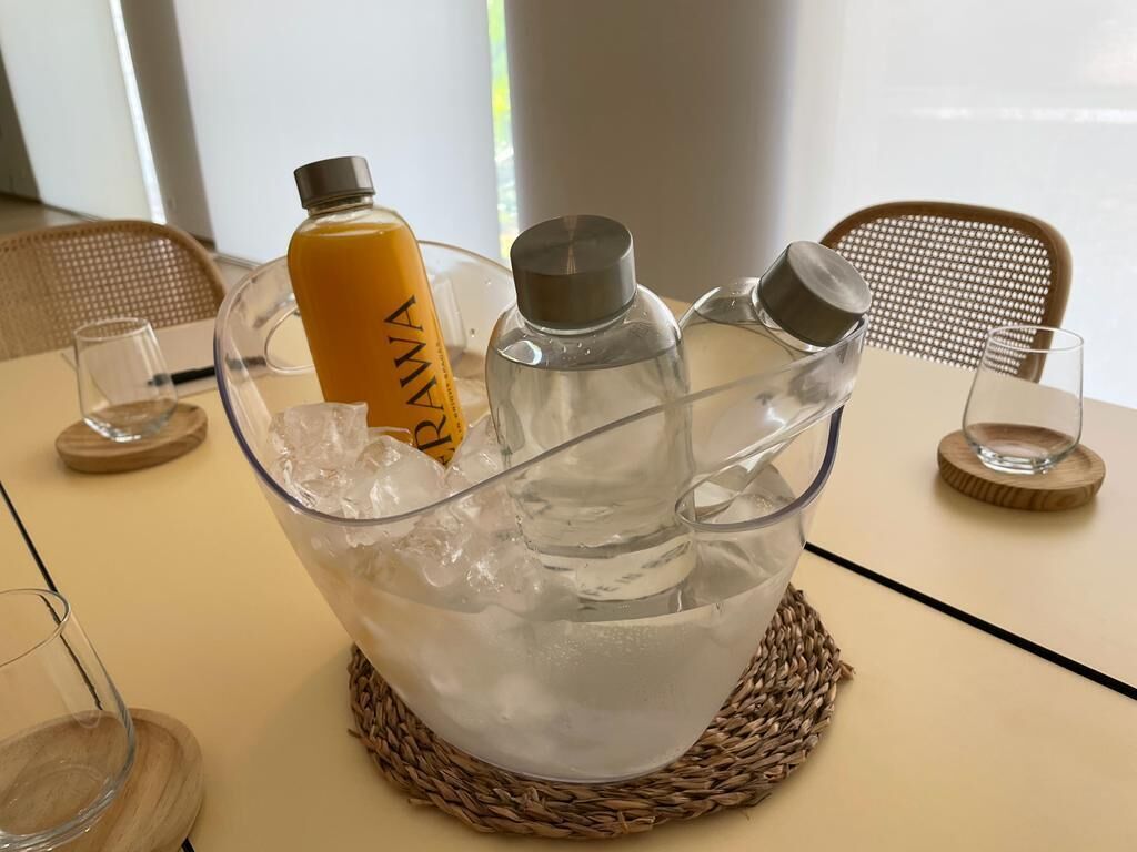 Un tazón de vidrio transparente lleno de hielo y agua, que contiene tres botellas con la etiqueta "RAWA".