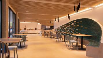 Een modern restaurantinterieur met houten plafondpanelen, zwarte hanglampen en een groene bakstenen muur. Tafels en stoelen staan klaar voor het diner.