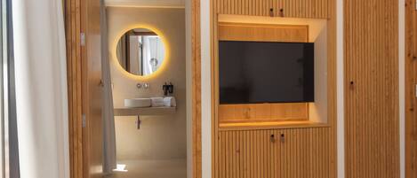 A modern bathroom with a wooden vanity, a round mirror, and a built-in TV.