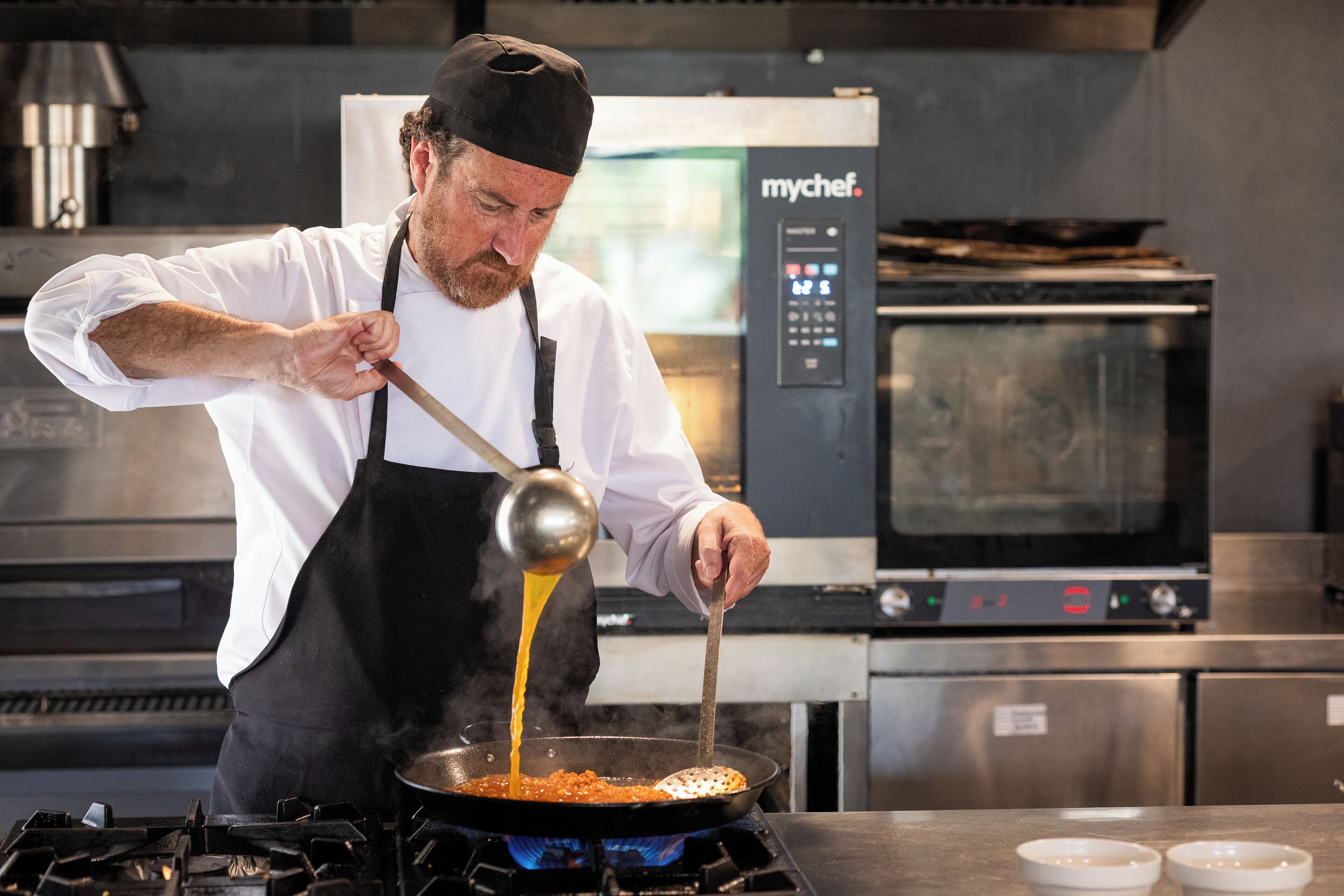 Un chef cuisinant dans une cuisine professionnelle équipée d’un four de marque et d’un panneau de commande numérique.