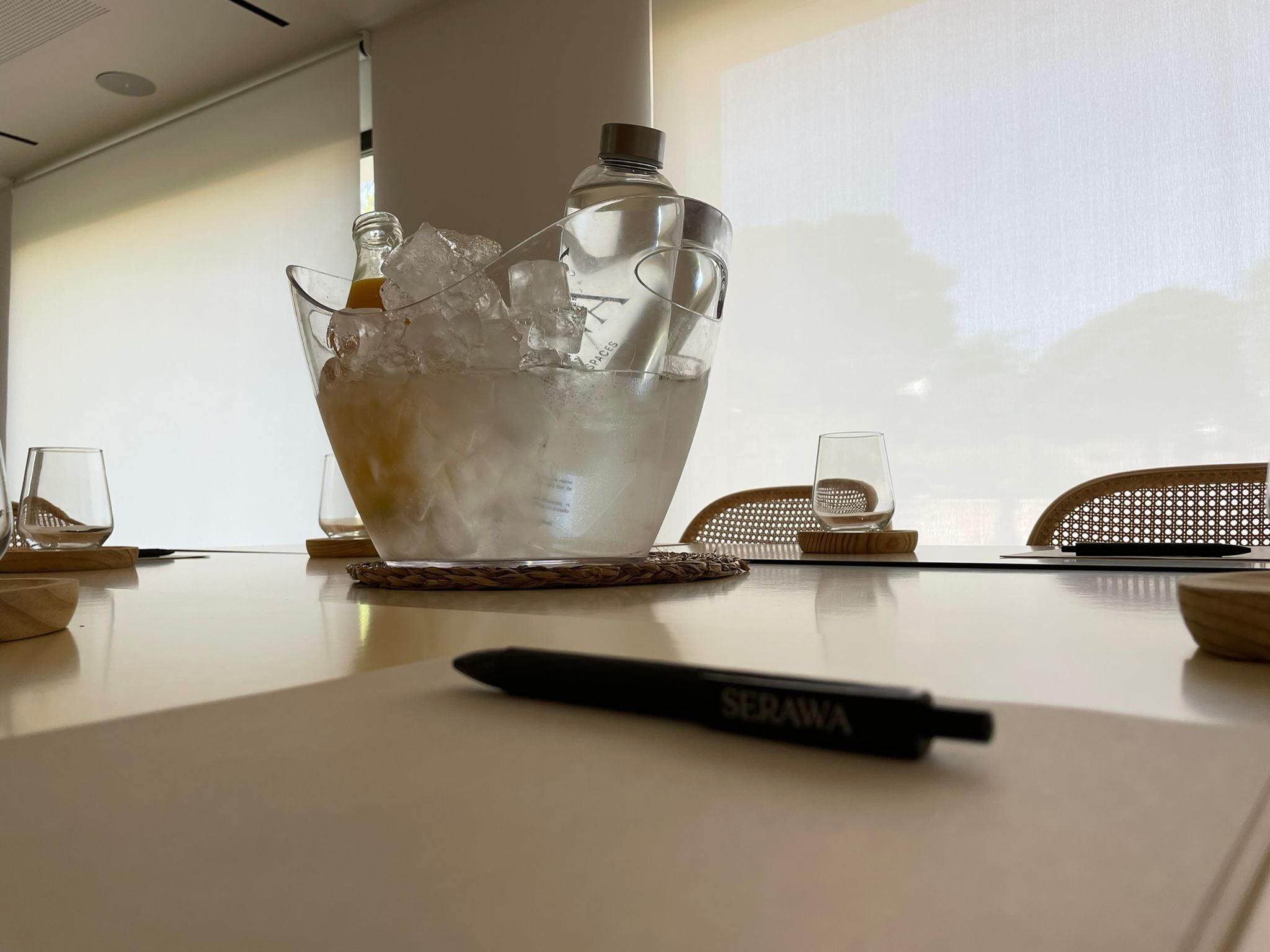 Une table de conférence sur laquelle se trouve un saladier en verre transparent contenant des glaçons et une bouteille, ainsi que deux verres, un stylo et, à l’arrière-plan, un écran de projecteur.