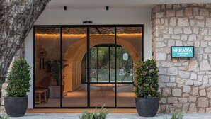 A modern hotel entrance with a stone wall, a glass door with a metal frame, and a sign reading "SERAWA". - Hotel Serawa Moraira (Teulada)