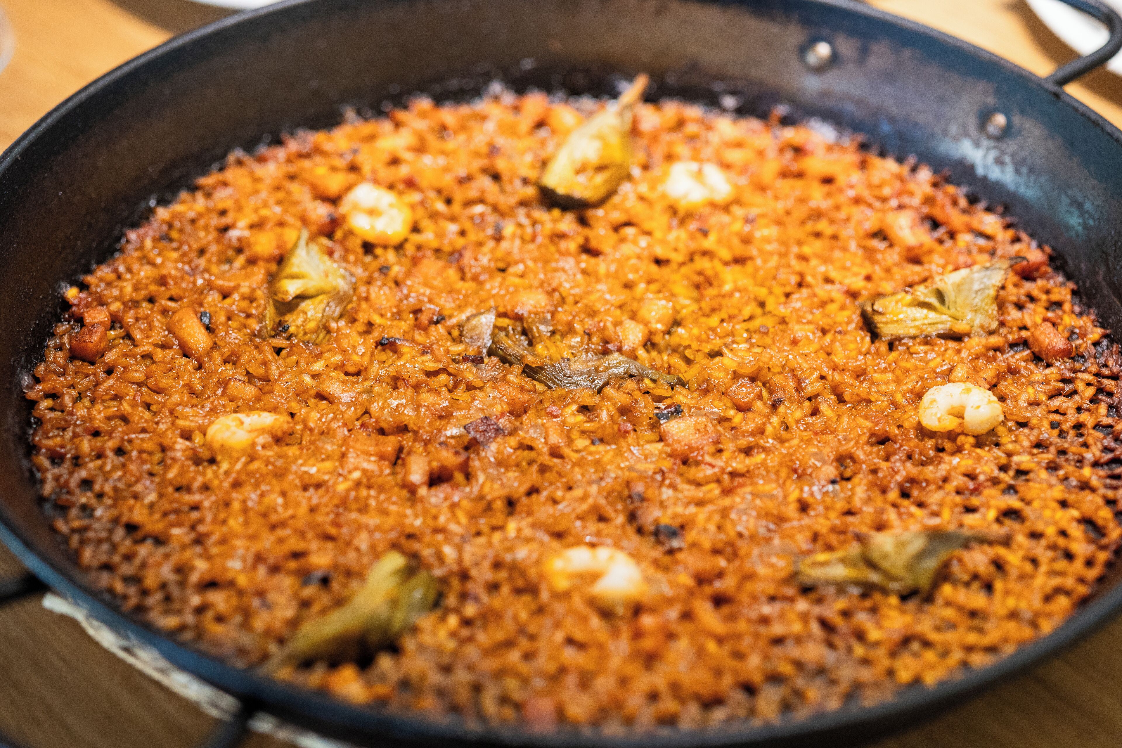 A large, shallow pan filled with a dish of rice, possibly a type of pilaf or rice-based meal, garnished with herbs and possibly seafood.