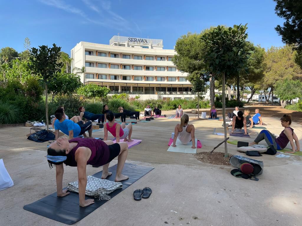 A group of people doing yoga outdoors in front of a hotel named SERAWA.