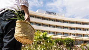 A person holding a woven basket with greenery, standing in front of a building labeled "SERAWA" with a garden in the background. - Hotel Serawa Moraira (Teulada)
