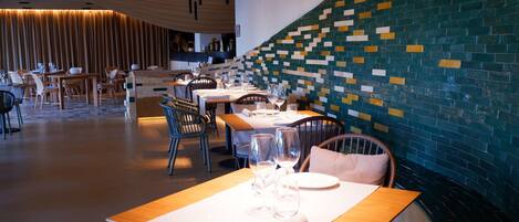 A modern restaurant with wooden tables and chairs, a patterned wall, and pendant lighting.