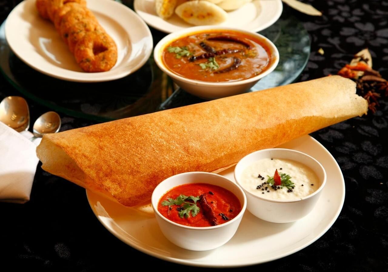 Un plato con una gran dosa, dos recipientes pequeños de chutney y una servilleta doblada.