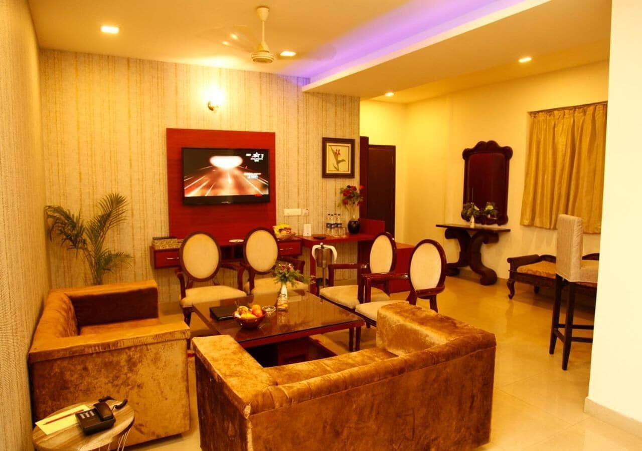 A hotel room with a living area featuring a sofa set, a coffee table, and a TV mounted on the wall.
