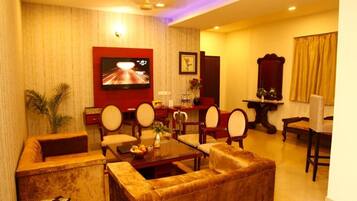 A hotel room with a living area featuring a sofa set, a coffee table, and a TV mounted on the wall.