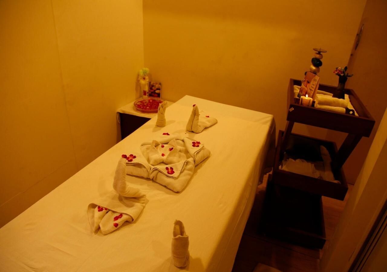 A hotel room with a neatly made bed, a small bedside table with a candle, and a wooden side table with toiletries.