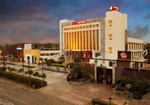 A hotel with a modern design, featuring a prominent bar and restaurant sign, a well-maintained garden, and a gated entrance. - MB Greens Clarks Inn Moradabad (Moradabad)