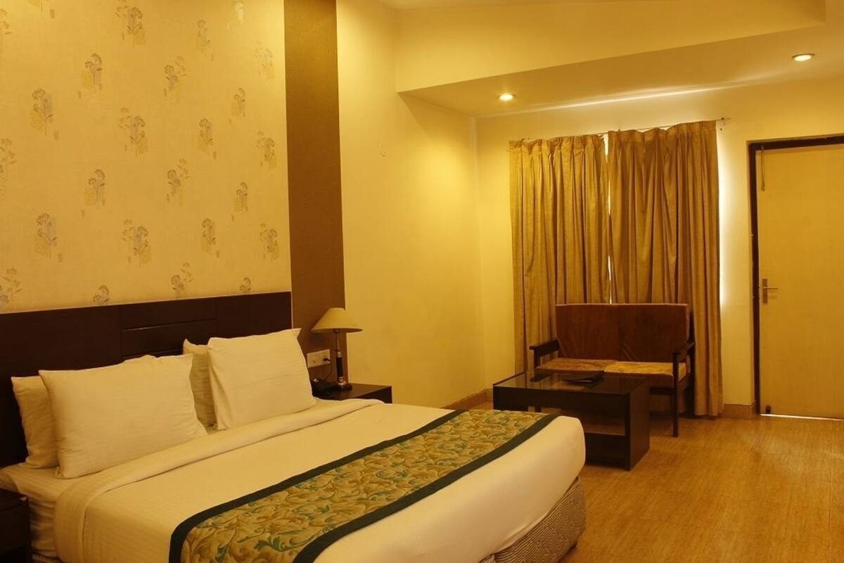 A hotel room with a bed, a desk, a chair, a lamp, and a curtain.