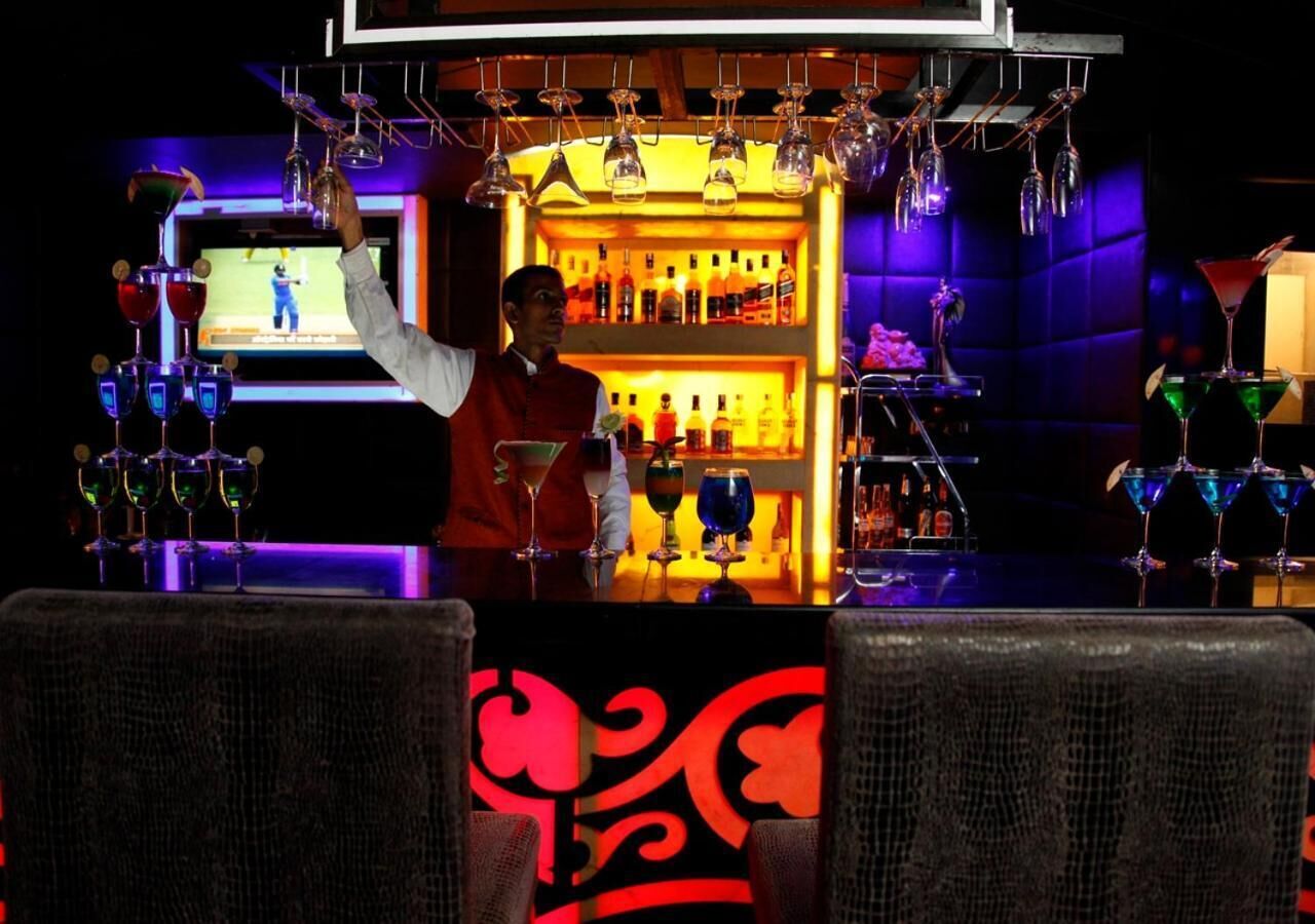 A bar area with a bartender, shelves of liquor bottles, and hanging light fixtures.