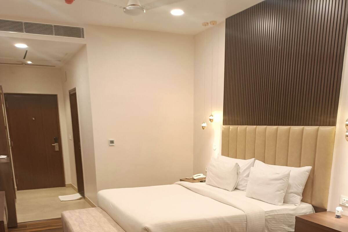 A modern hotel room with a large bed, bedside tables, a wooden floor, and a ceiling fan.