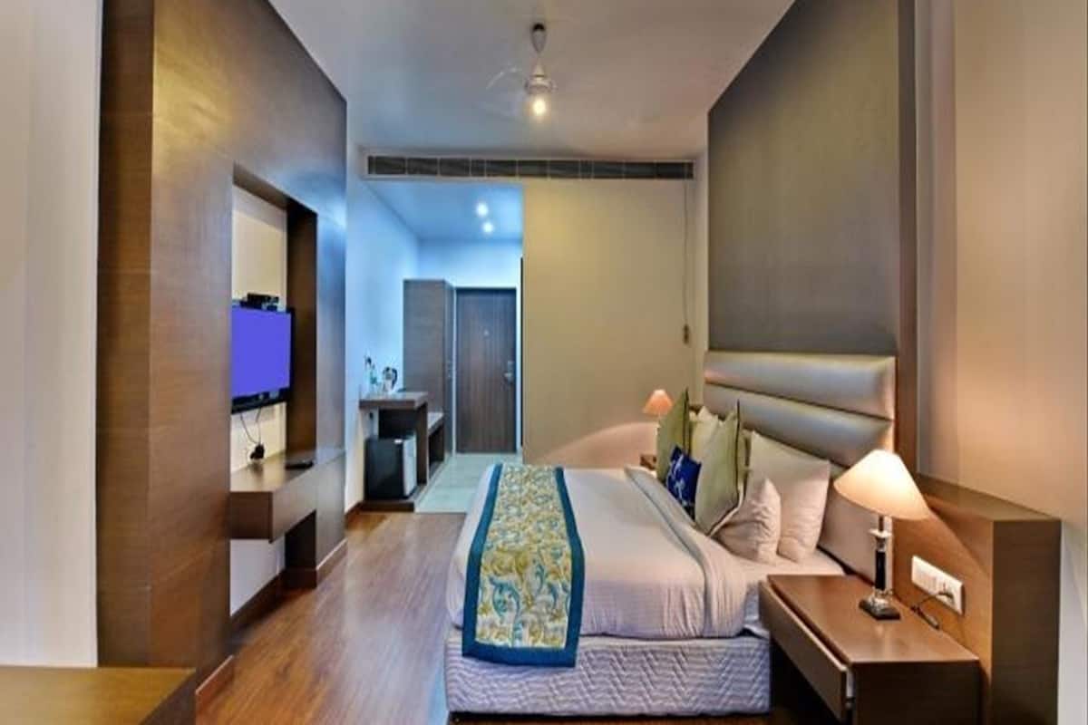A modern hotel room with a large bed, bedside tables, a television, and a bathroom visible through an open door.
