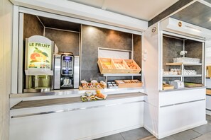 A breakfast bar with a coffee machine, a fruit display, and a pastry case.