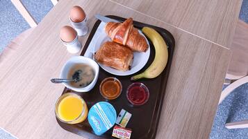 A tray with croissants, a banana, a croissant sandwich, a cup of coffee, a glass of orange juice, jam, and a packet of instant coffee.