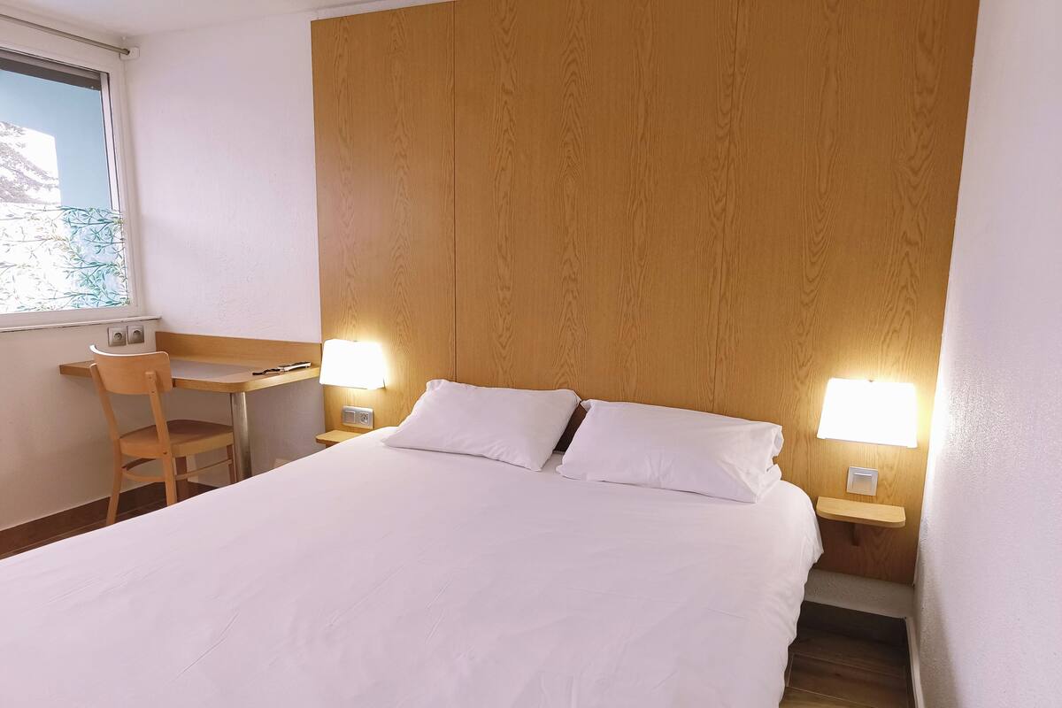 A hotel room with a bed, a desk, and two bedside lamps.