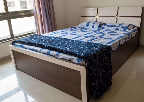 Una cama con cabecera, una ventana con cortinas y piso de baldosas.