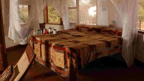 A bedroom with a large bed, a window, and a chair. - Leopard Rock Lodge (Meru National Park)