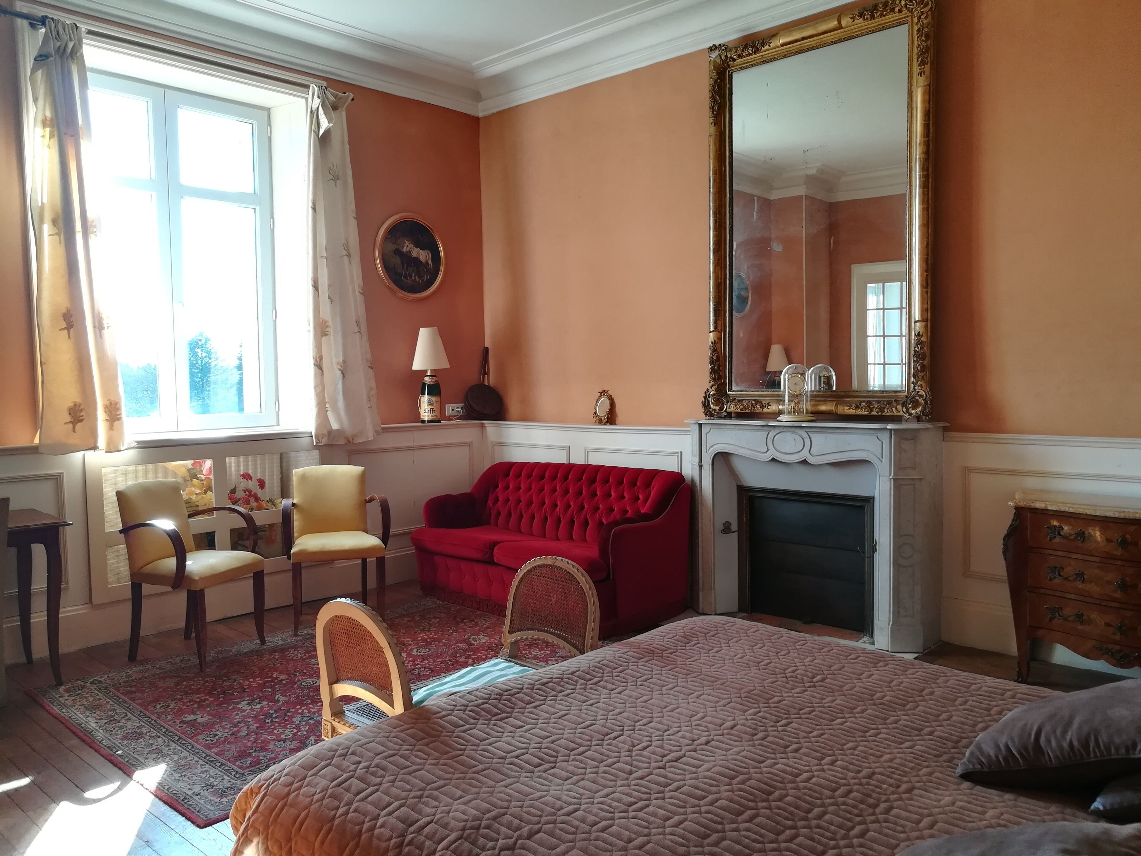 Une chambre d’hôtel avec un grand lit, un canapé rouge, une cheminée et un grand miroir.