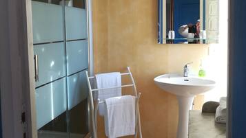 A bathroom with a glass shower enclosure, a white towel rack, a sink with a mirror above it, and a blue door in the background.