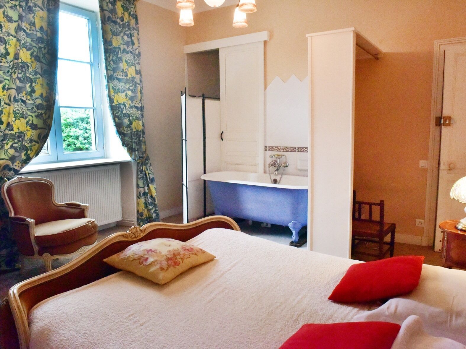 Une chambre à coucher avec un lit, une chaise, une salle de bain avec une baignoire et une fenêtre avec des rideaux.