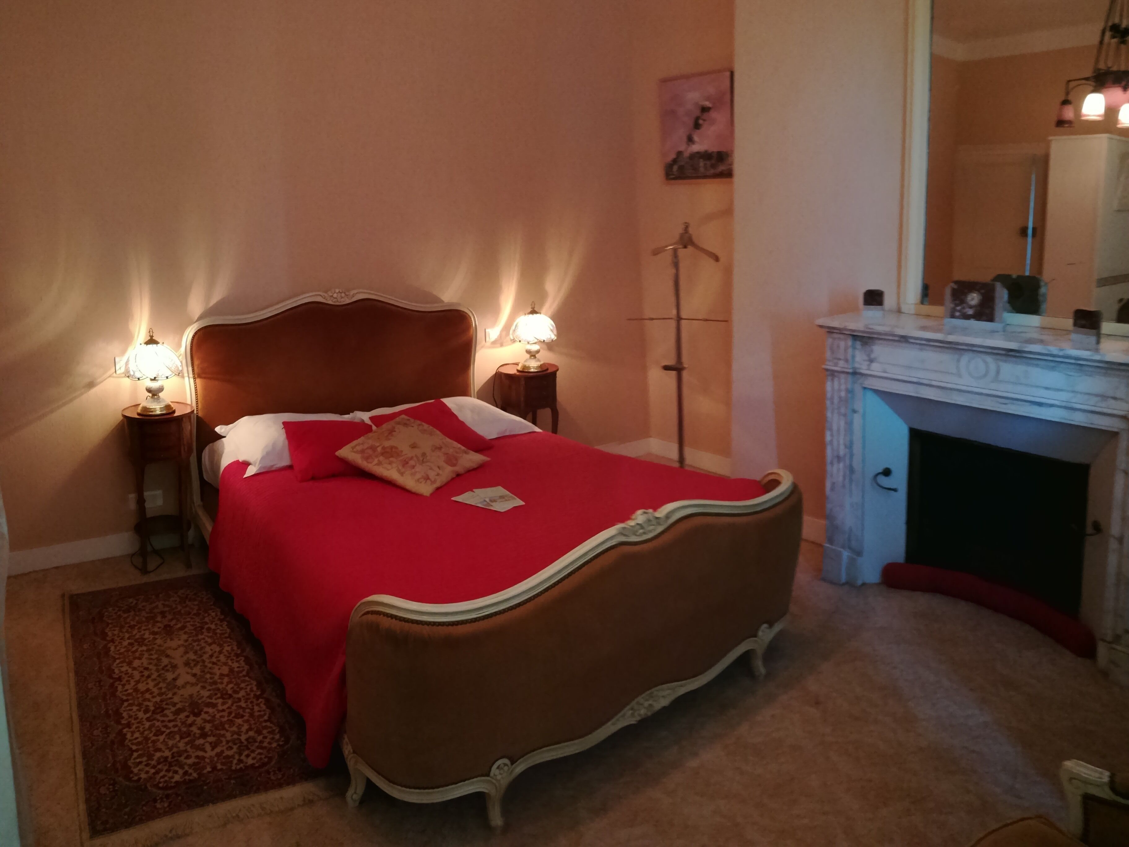 Ein Schlafzimmer mit einem großen Bett, zwei Nachttischen mit Lampen, einer Stehlampe, einem Kamin und einem Bild an der Wand.