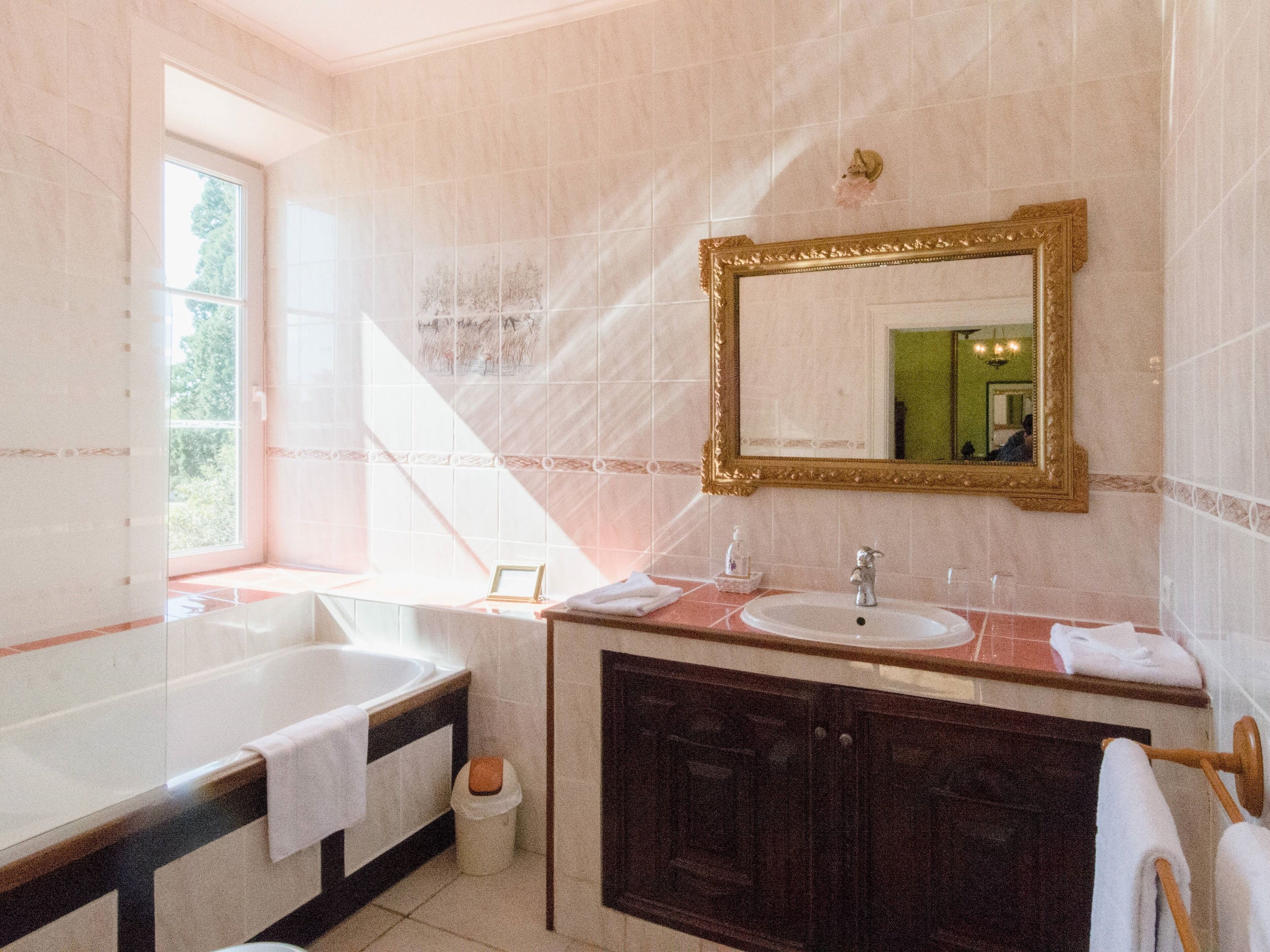 A bathroom with a large bathtub, a sink, and a vanity with a mirror. There is a window providing natural light.