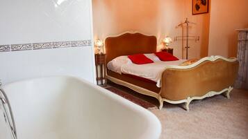 A bedroom with a large white bathtub, a bed with red pillows, and a floor lamp.