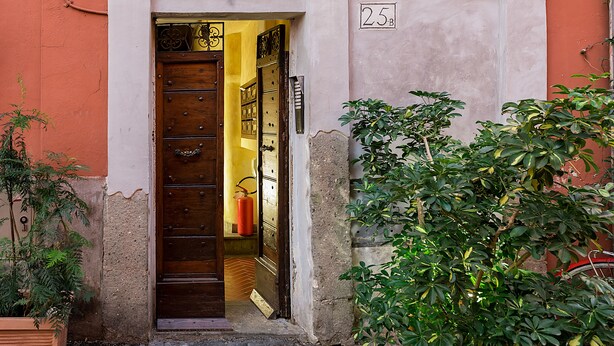Entrada de un edificio con una puerta de madera, un extintor en el interior y una placa con un número.