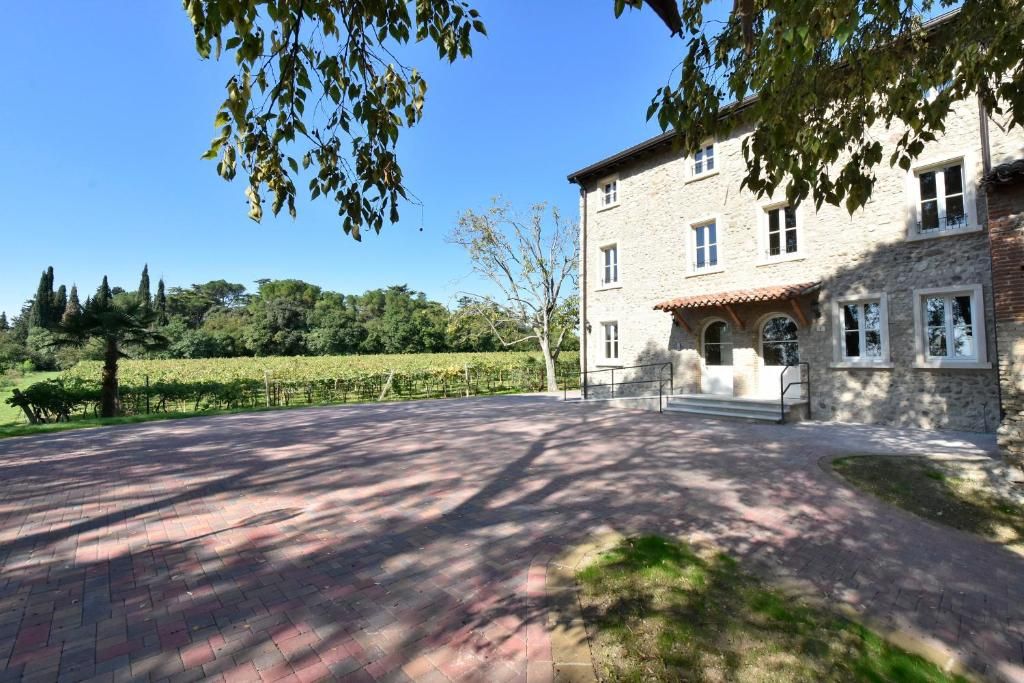 En bygning i sten med en belagt indkørsel og en vingård i baggrunden.