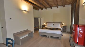 A bedroom with a bed, bedside tables, a chair, a small table, a red appliance, and a wooden ceiling.