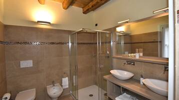 A modern bathroom with a glass-enclosed shower, two sinks, and a bidet.