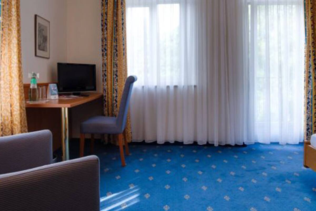 A hotel room with a bed, a desk with a computer, a chair, and a television.
