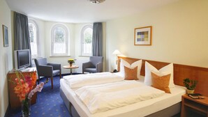 A hotel room with a large bed, two chairs, a small table, a TV, and a window with curtains. - AKZENT Hotel Johannisbad (Bad Aibling)