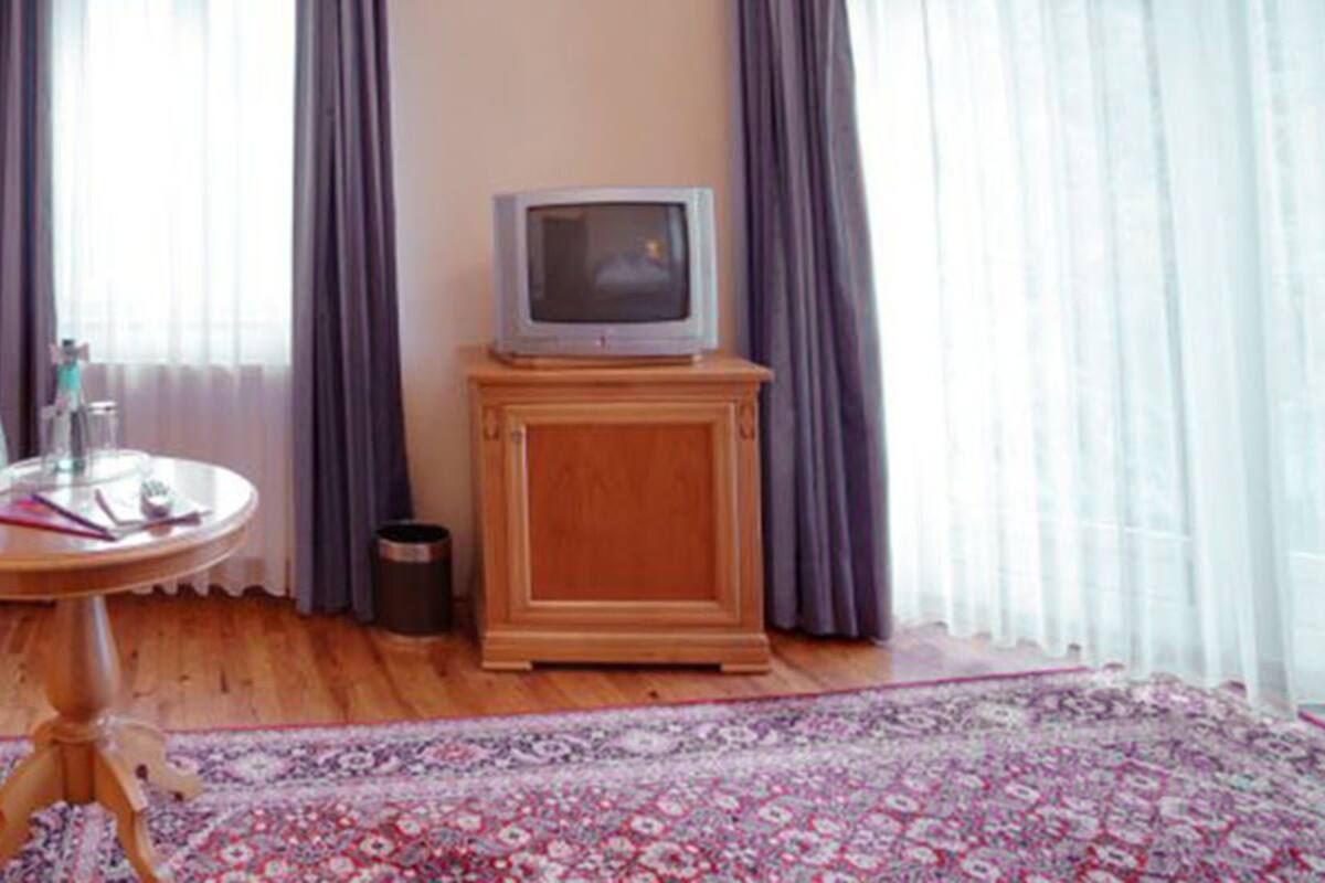 A living room with a striped sofa, a small round table, a television on a wooden cabinet, and a patterned rug.