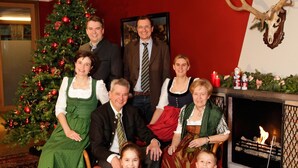 A family posing in a room with a Christmas tree, a fireplace, and a mounted deer head. - AKZENT Hotel Johannisbad (Bad Aibling)