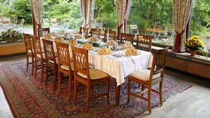 A dining area with a long table set for a meal, surrounded by chairs, with a view of greenery outside. - AKZENT Hotel Johannisbad (Bad Aibling)