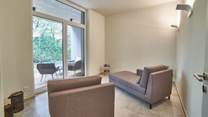 En moderne stue med sofa og stole, en skydedør til et udendørs område og et lille sofabord.