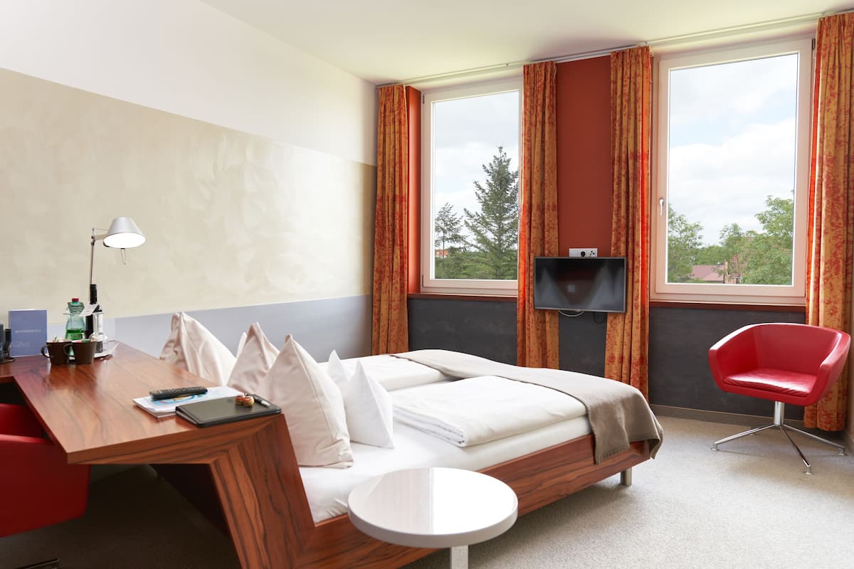 A hotel room with a bed, a desk with a lamp, a chair, and a TV.