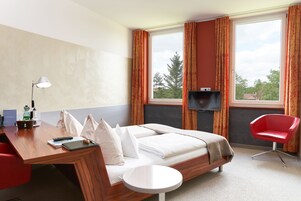 Habitación de hotel con una cama, un escritorio con lámpara, una silla y un televisor.