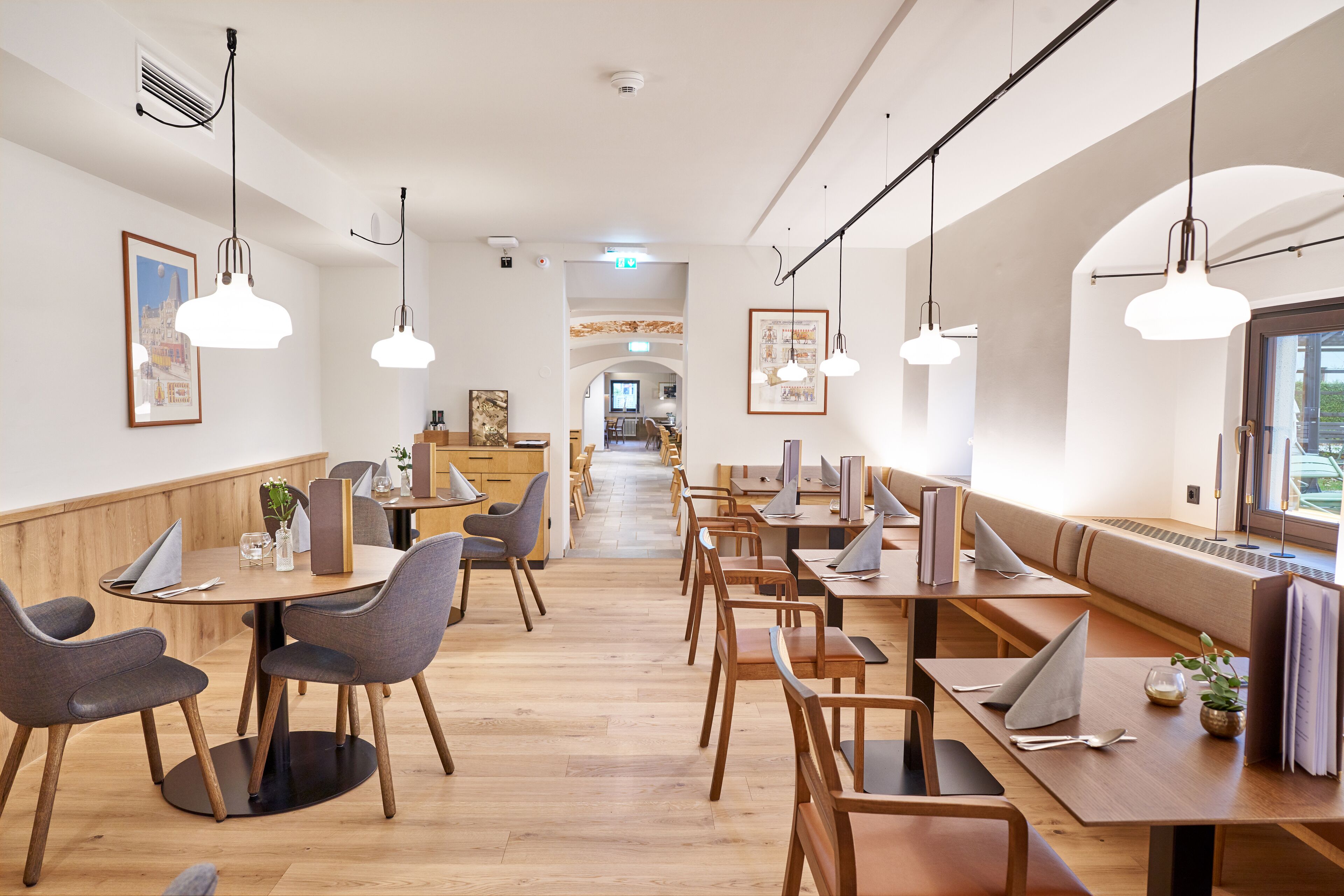 A modern dining area with wooden tables and chairs, pendant lighting, and framed artwork on the walls.
