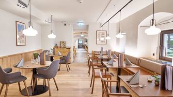 A modern dining area with wooden tables and chairs, pendant lighting, and framed artwork on the walls.