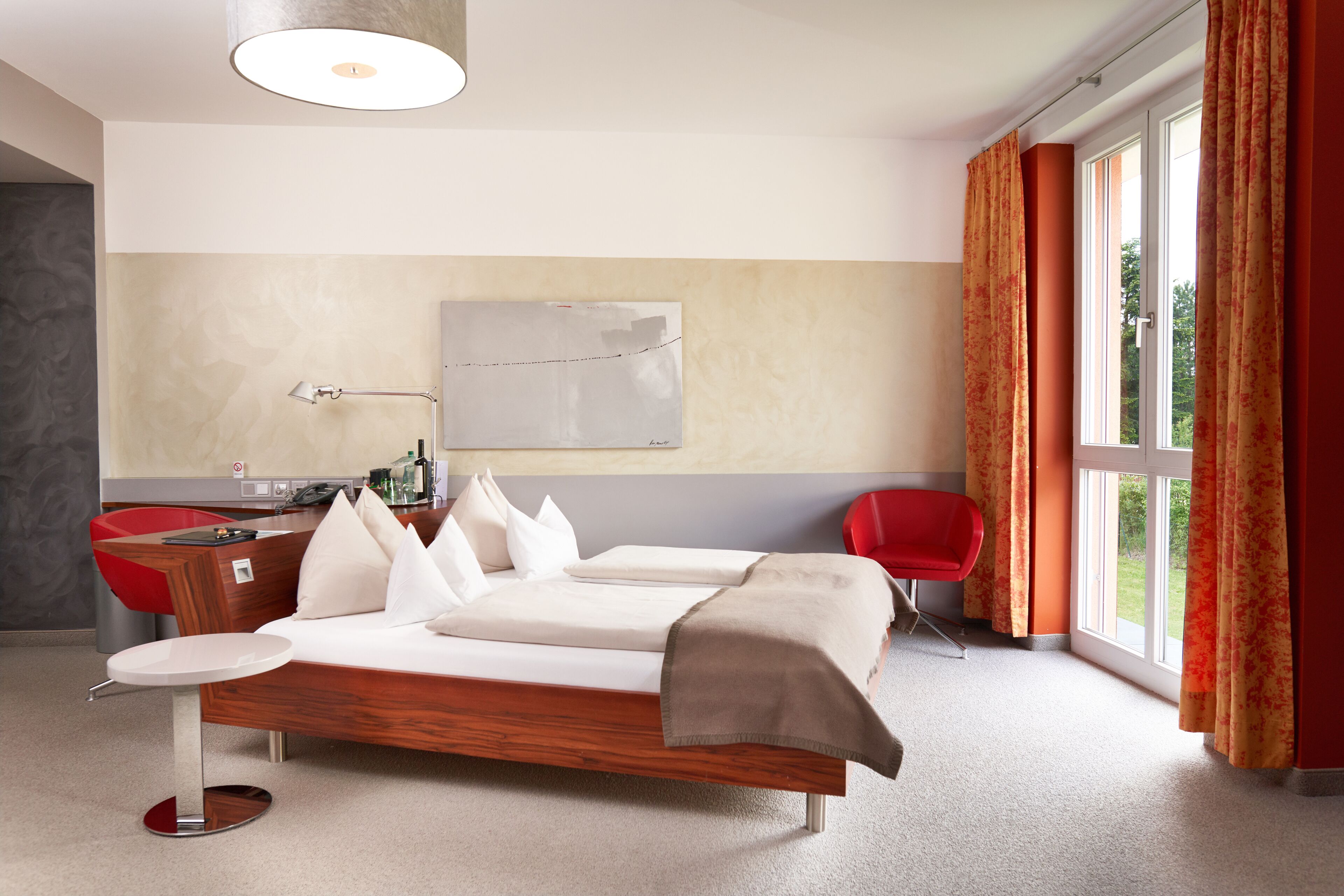 A modern hotel room with a wooden bed, a desk, a chair, and a large window with curtains.