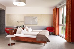 Una habitación de hotel moderna con una cama de madera, un escritorio, una silla y un ventanal con cortinas.