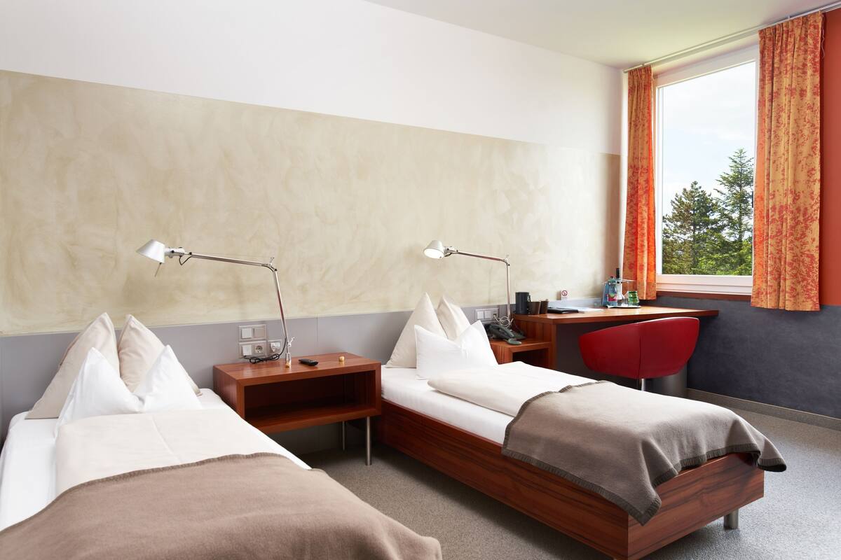 A hotel room with two beds, a desk, a chair, and a window with curtains.