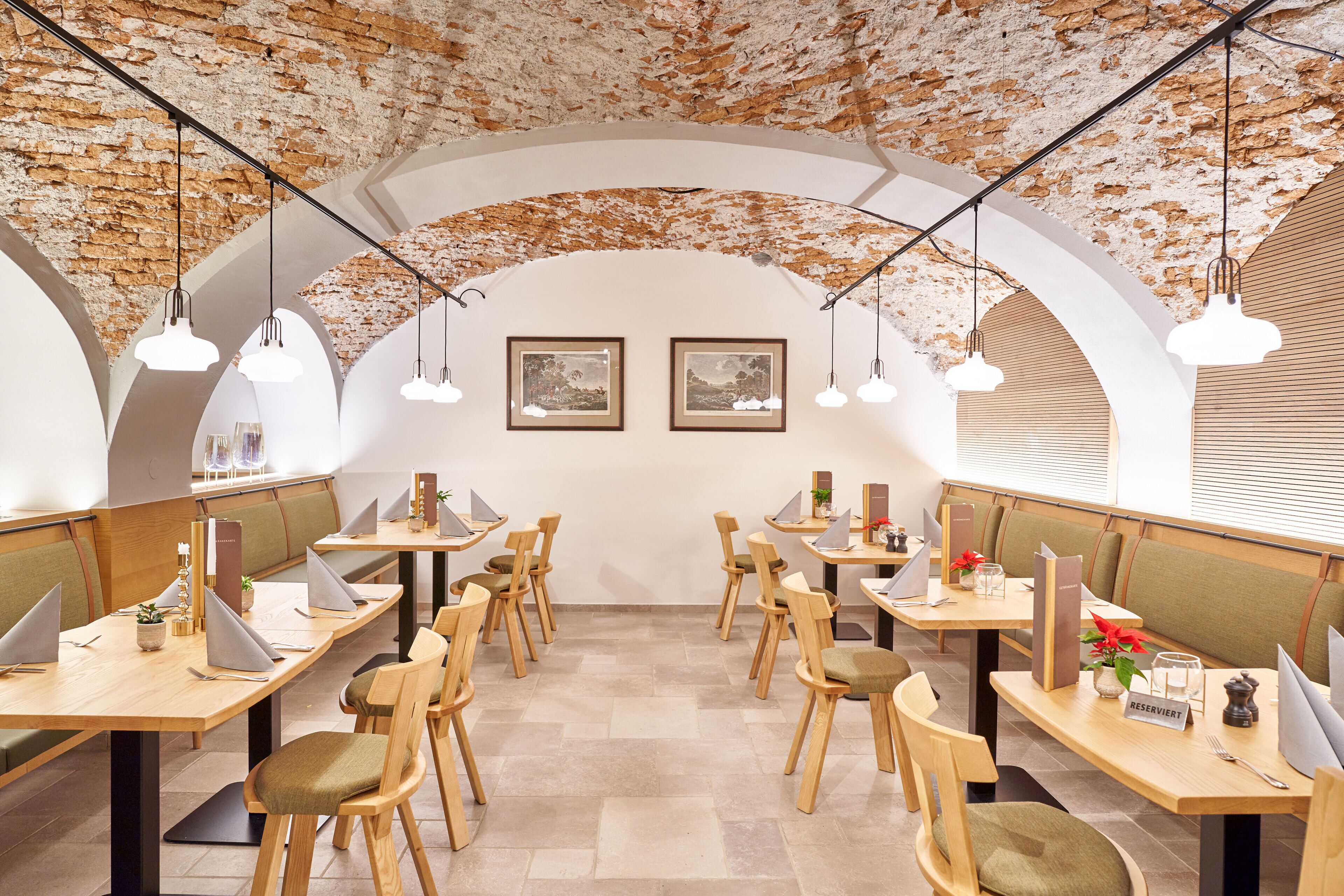 A restaurant with wooden tables and chairs, white walls, and a brick ceiling.