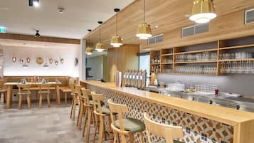 Un espace bar avec des meubles en bois, des luminaires suspendus et des étagères remplies de verres.